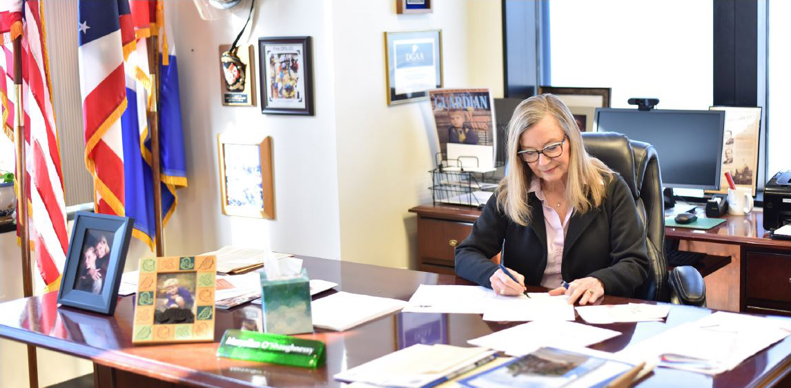 Clerk O’Shaughnessy signing documents at her desk.